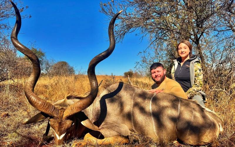 Harvested white tail deer laying on the ground with a rifle laying across its side after a successful Texas whitetail deer hunt.